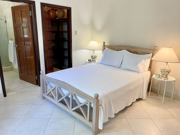 A neatly made bed with white linens, a wooden headboard, and two bedside lamps. - Family-Friendly 3BR Villa Apartment w/ Pool – Steps to Surf & Ocean (Green Garden)