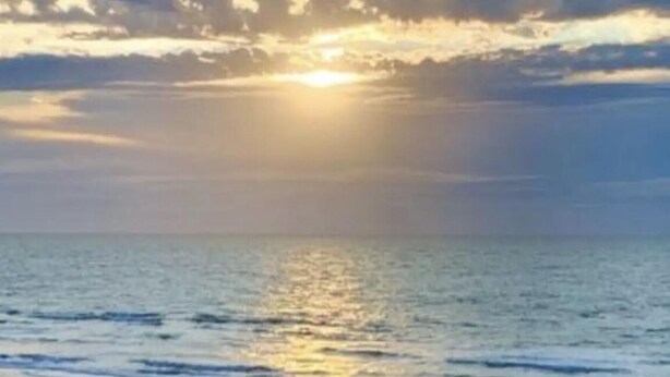 Ein Strandbild mit einem Sonnenuntergang über dem Meer.