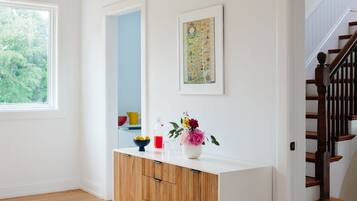 Una habitación moderna con suelo de madera, paredes blancas, un mueble blanco, un ventanal grande y una escalera.