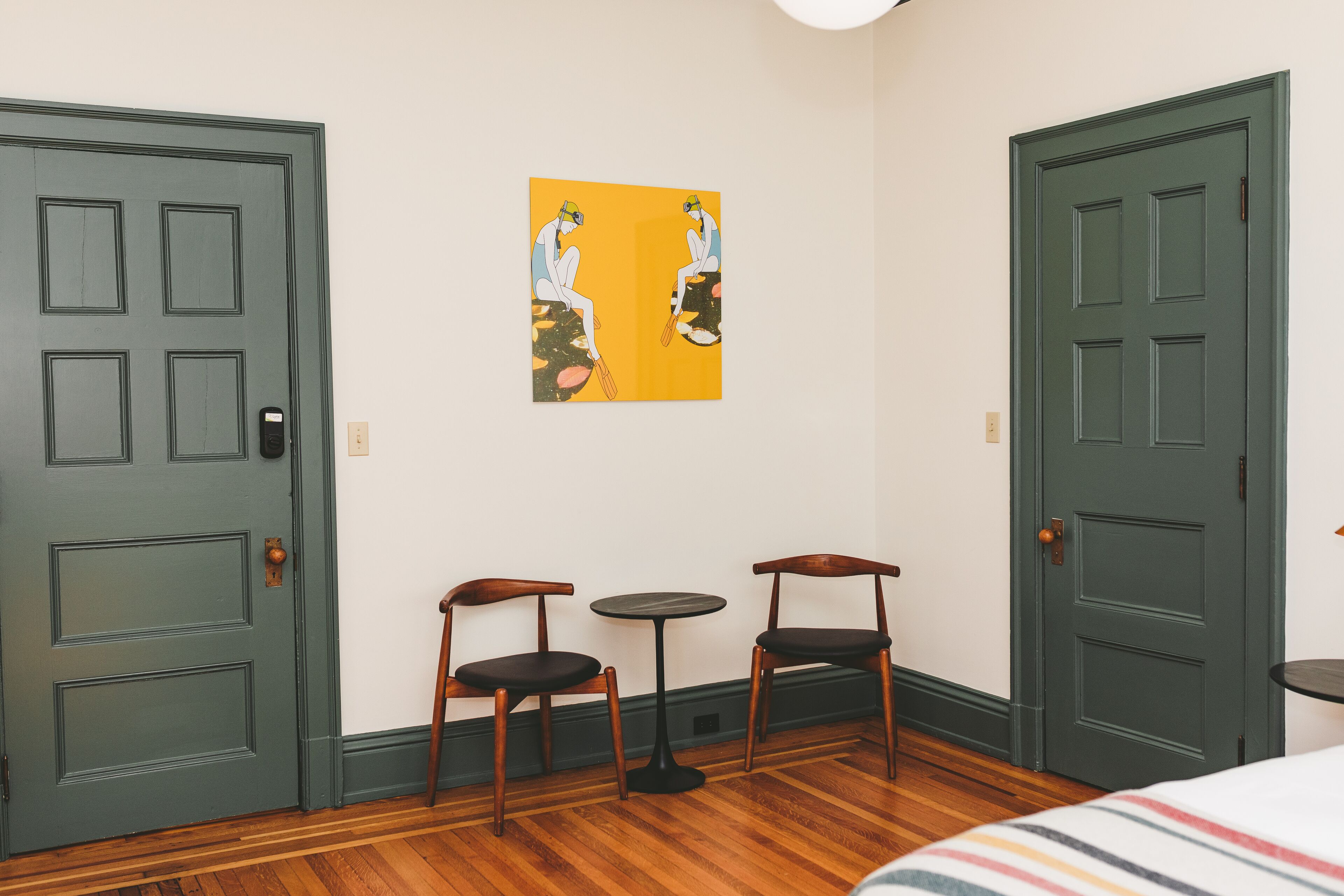 Ein Zimmer mit zwei Türen, einem kleinen Tisch, zwei Stühlen und einem Bild an der Wand.