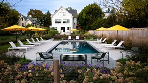 A swimming pool with lounge chairs and umbrellas, surrounded by a fence and flowers. - The Amelia (Hudson)
