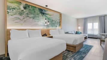 A hotel room with two beds, a large abstract painting, a desk, and a chair.