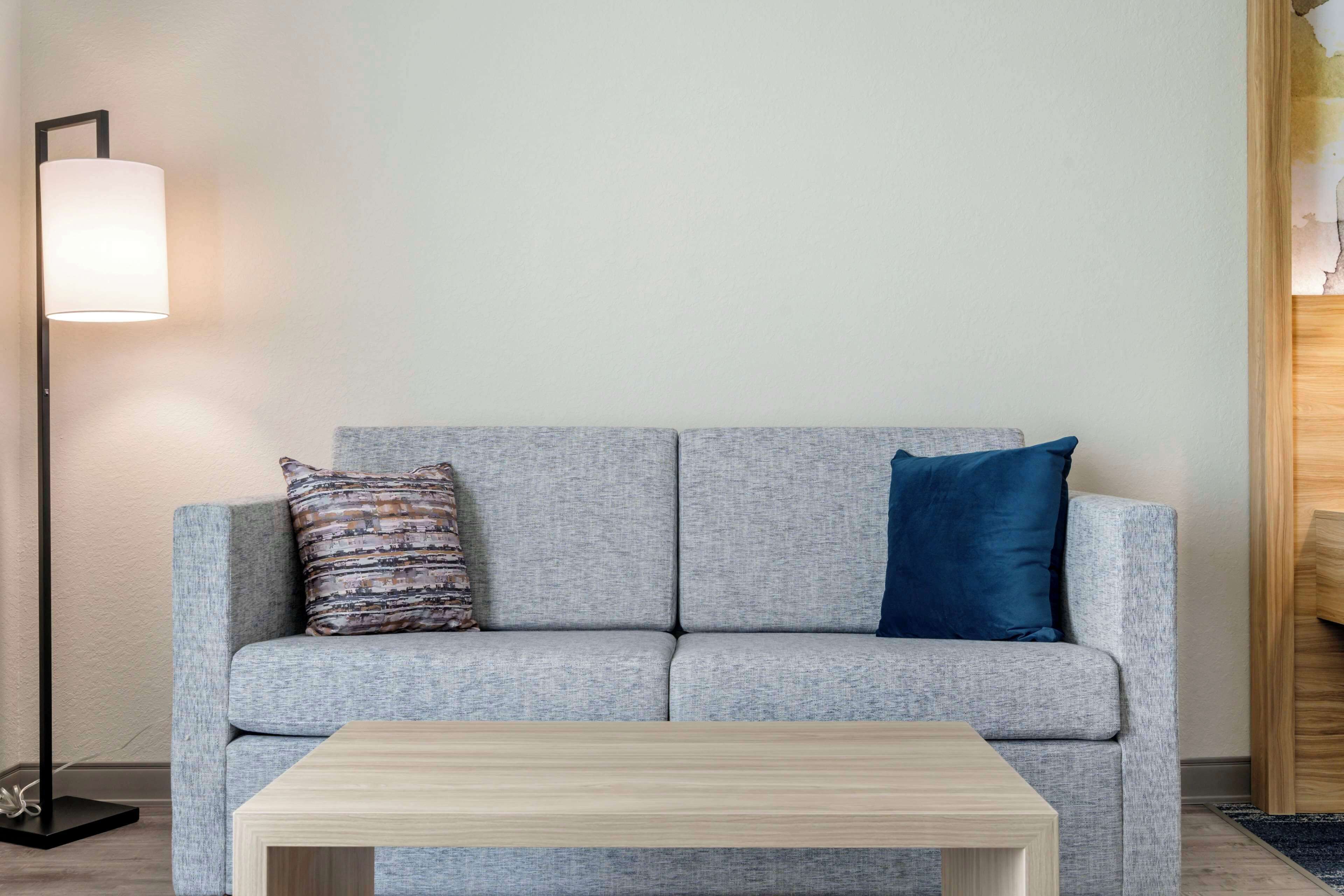 Un sofá gris con dos almohadones, una mesita de centro de madera y una lámpara de pie.