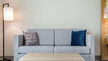 Un sofá gris con dos almohadones, una mesita de centro de madera y una lámpara de pie.