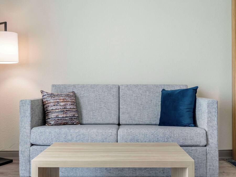 Un sofá gris con dos almohadones, una mesita de centro de madera y una lámpara de pie.
