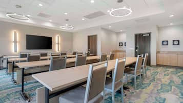 A conference room with long tables, chairs, a flat-screen TV, and a patterned carpet.