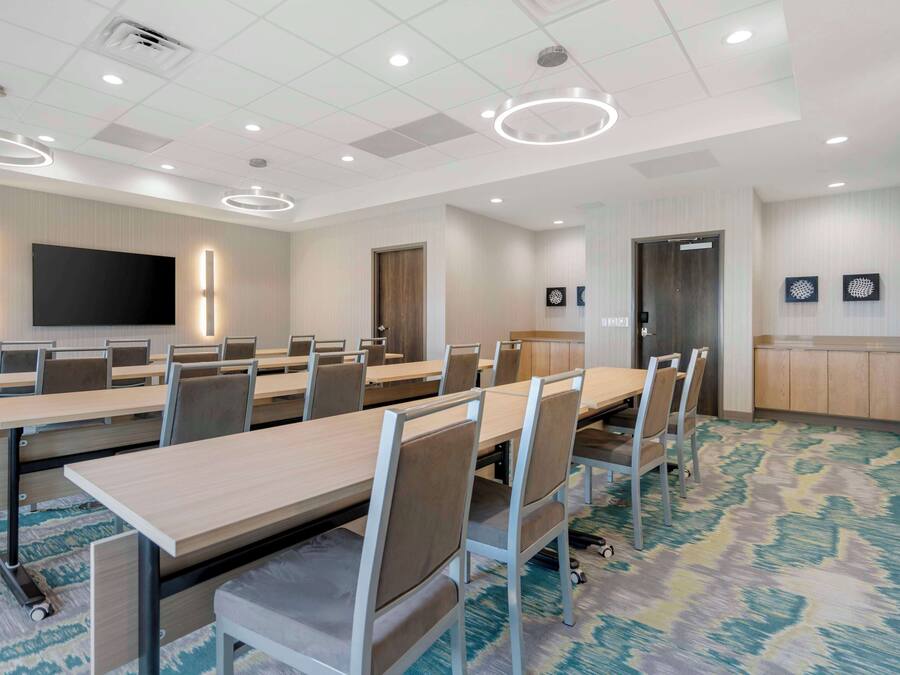 A conference room with long tables, chairs, a flat-screen TV, and a patterned carpet.