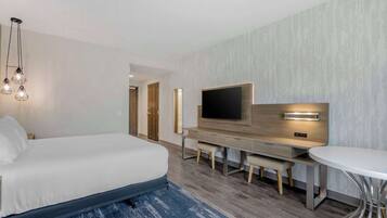 A modern hotel room with a large bed, a desk with a flat-screen TV, and a round dining table.