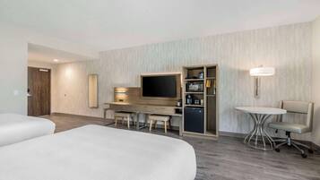 Een hotelkamer met twee bedden, een bureau met een televisie, een minibar en een kleine tafel met een stoel.