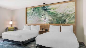 A hotel room with two beds, a large abstract painting on the wall, a bedside table with a lamp, and a modern light fixture.
