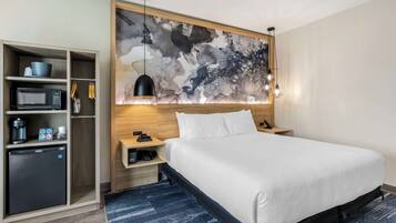 A hotel room with a bed, a desk, a microwave, a mini-fridge, and a shelf with toiletries.
