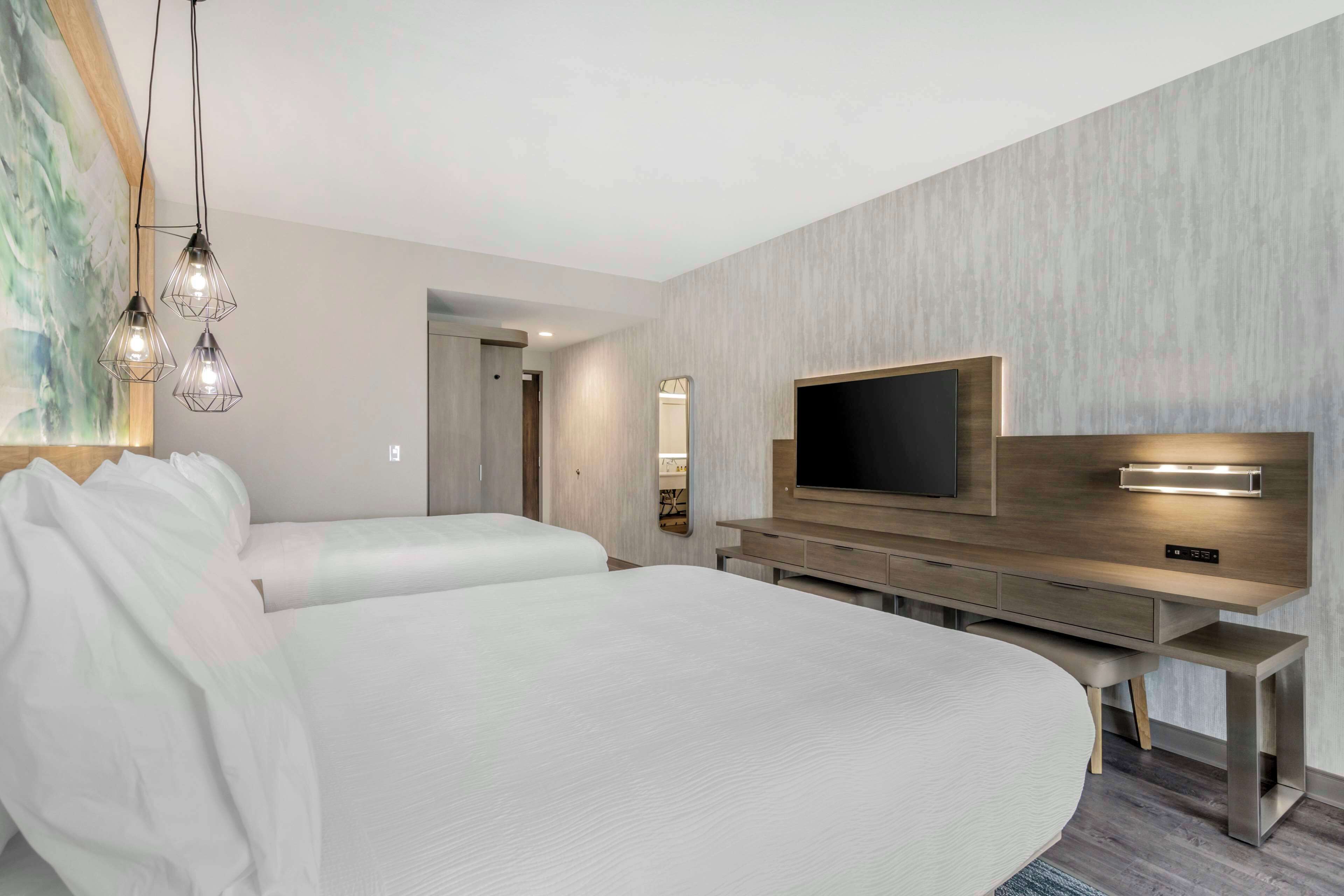 A modern hotel room with a large bed, a TV, and a desk with drawers.