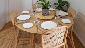 Una mesa de madera redonda con platos blancos, cubiertos y un jarrón decorativo con flores.