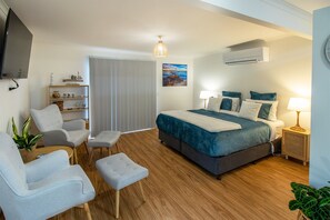 A modern bedroom with a large bed, bedside lamps, a television, and a view of the outdoors. - Delightful studio situated in a koala corridor (Mallacoota)