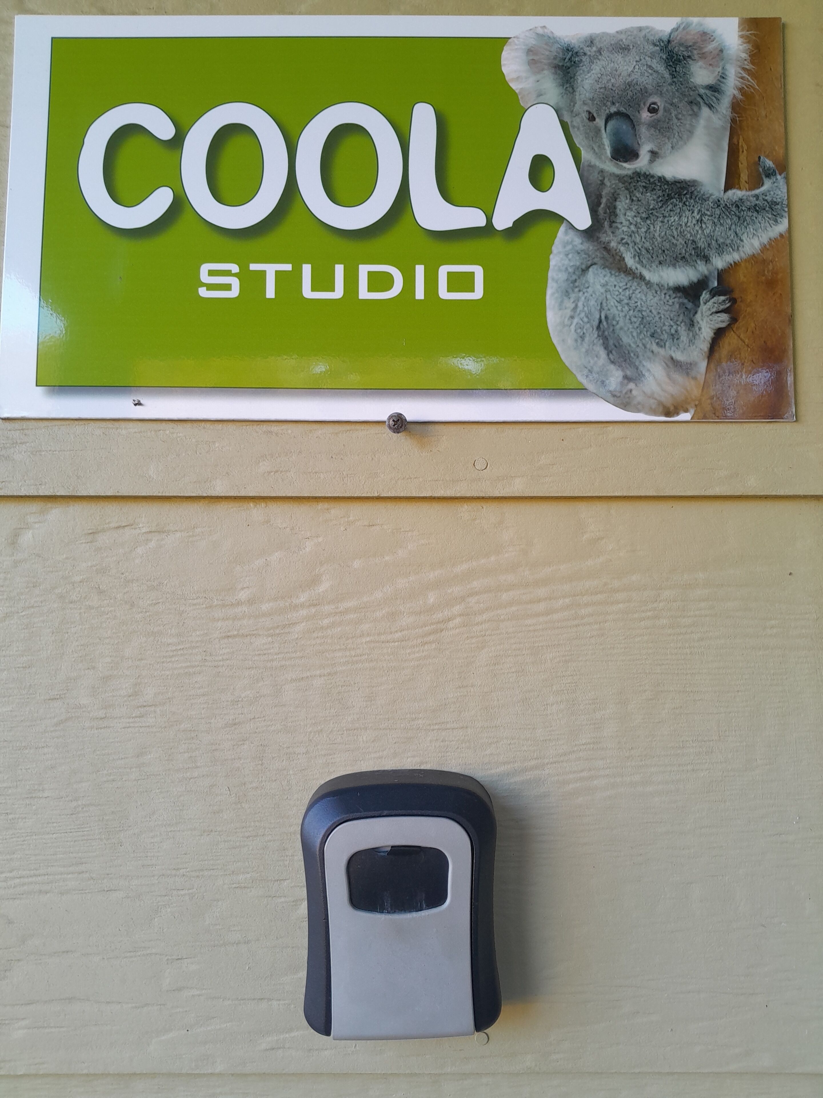 Une enseigne représentant un koala et portant l’inscription « COOLA STUDIO ». En dessous, on aperçoit un objet noir, qui pourrait être un téléphone ou une télécommande.