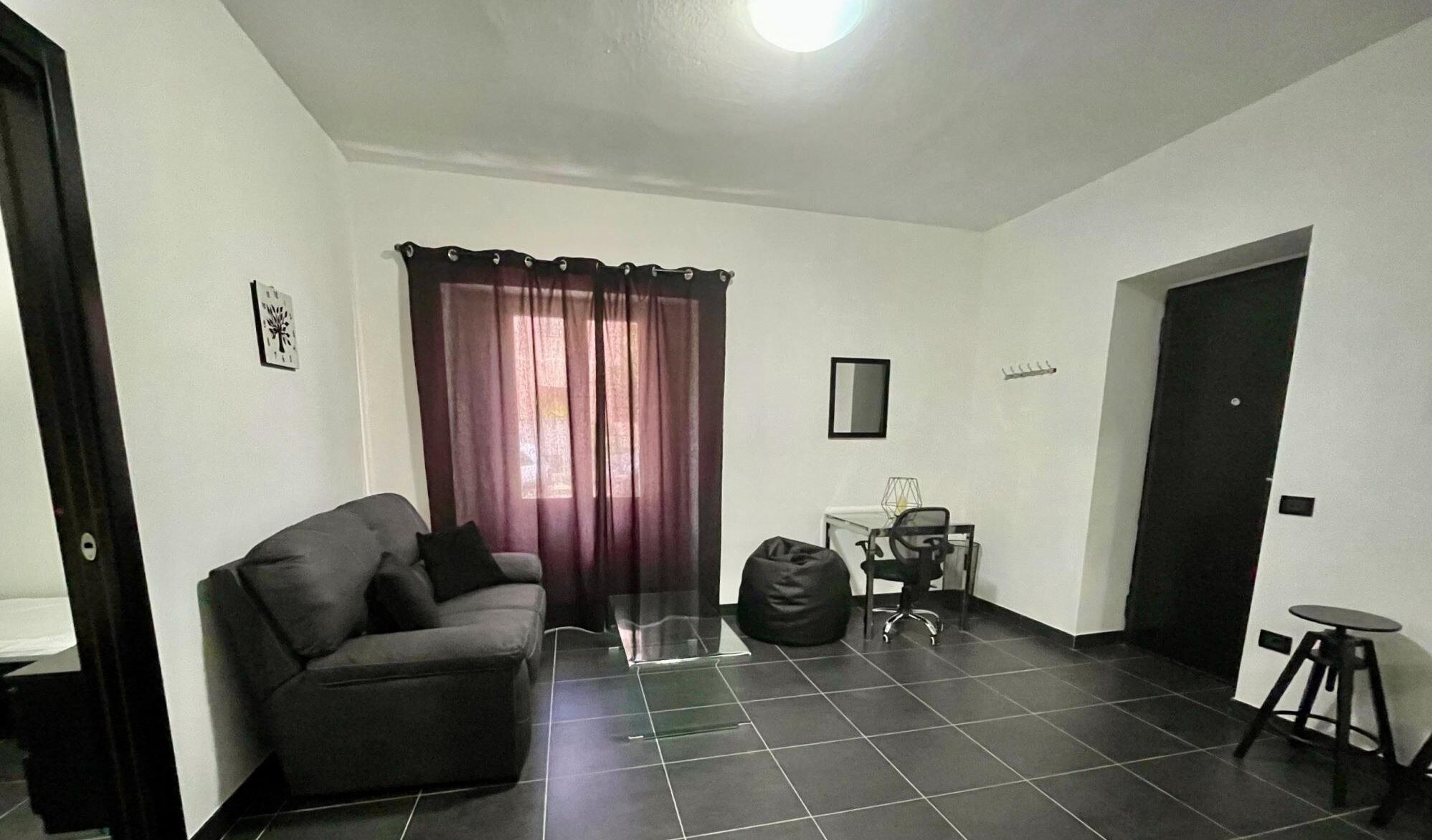 Ein Wohnzimmer mit einer Couch, einem Glastisch, einem Sessel, einem kleinen Tisch und einer Tür.