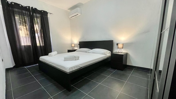 A modern hotel room with a large bed, two bedside tables, an air conditioning unit, and a view of the outdoors through the window. - Bonaventura s House by Wonderful Italy (Olbia)