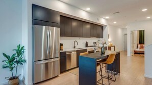 A modern kitchen with a stainless steel refrigerator, dark cabinetry, and a central island with bar stools.