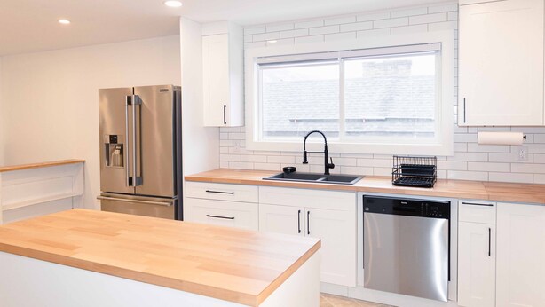 A modern kitchen with white cabinetry, stainless steel appliances, and a wooden countertop. - Beautiful quiet space located in the heart of Merritt suburbs. (Merritt)
