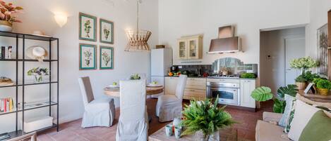 A modern kitchen with white cabinets, a wooden ceiling, and a dining area with chairs and a table.