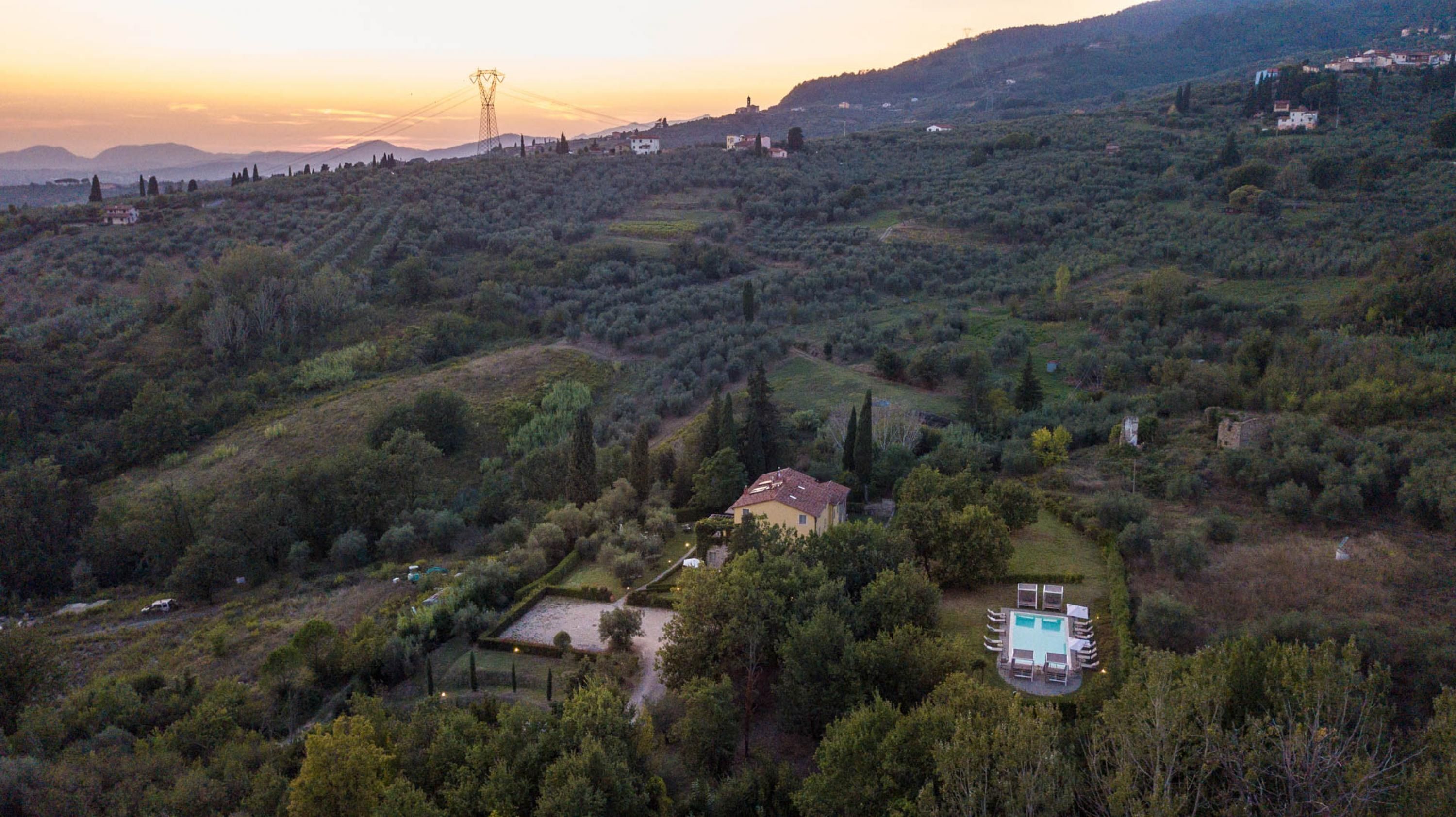 A rural landscape with a house surrounded by trees, a swimming pool, and distant hills.