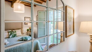 A bedroom with a large window, a bed with a quilted cover, a bedside table with a lamp, and a framed picture on the wall. - Casa Pinocchio at Borghetto Farmhouse (Capannori)