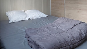 Un dormitorio con cama, dos almohadas blancas y una colcha gris.