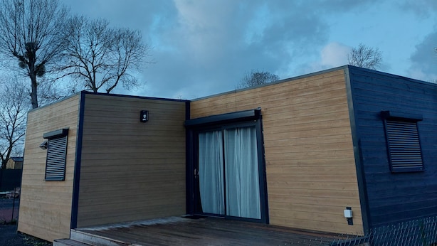 Una cabaña de madera moderna de dos pisos con un porche de madera y un amplio ventanal corredera.