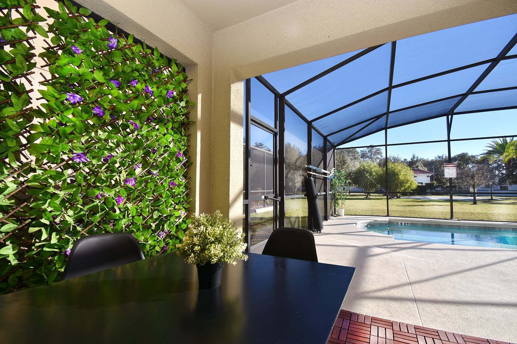 Eine überdachte Terrasse mit Pool, einem Tisch mit Stühlen sowie eine Wand mit Kletterpflanzen und Blumen.