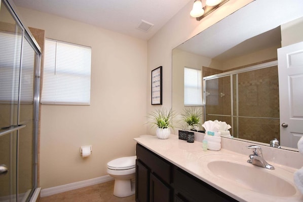 A bathroom with a toilet, sink, mirror, and shower. - Family Getaway: Game Room, Themed Rooms & Private Yard Near Disney, BBQ!! (Kissimmee)