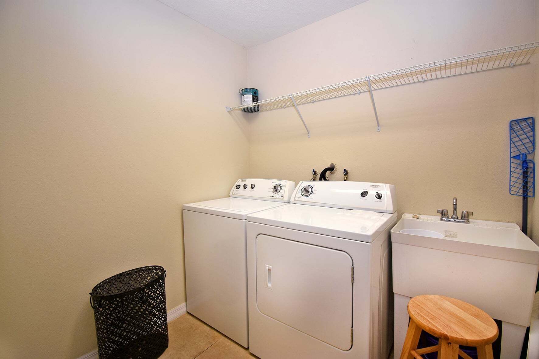 A laundry room with a washer and dryer, a sink, a stool, and a shelf with a can.