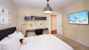 Un dormitorio con cama, escritorio, silla, lámpara en el techo y televisión montada en la pared.