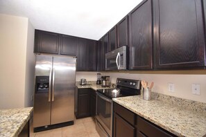 A kitchen with dark wooden cabinets, stainless steel appliances, granite countertops, and a built-in microwave. - Family Getaway: Game Room, Themed Rooms & Private Yard Near Disney, BBQ!! (Kissimmee)