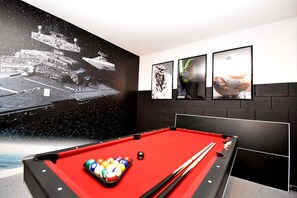 A pool table with balls and cues, a large space-themed mural, and three framed pictures on the wall.