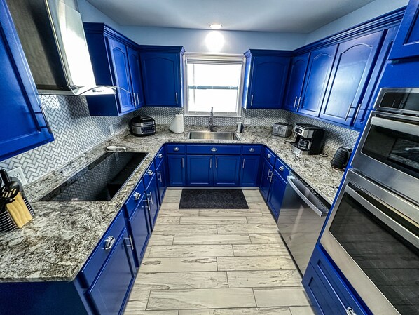 A modern kitchen with blue cabinets, a granite countertop, and stainless steel appliances.