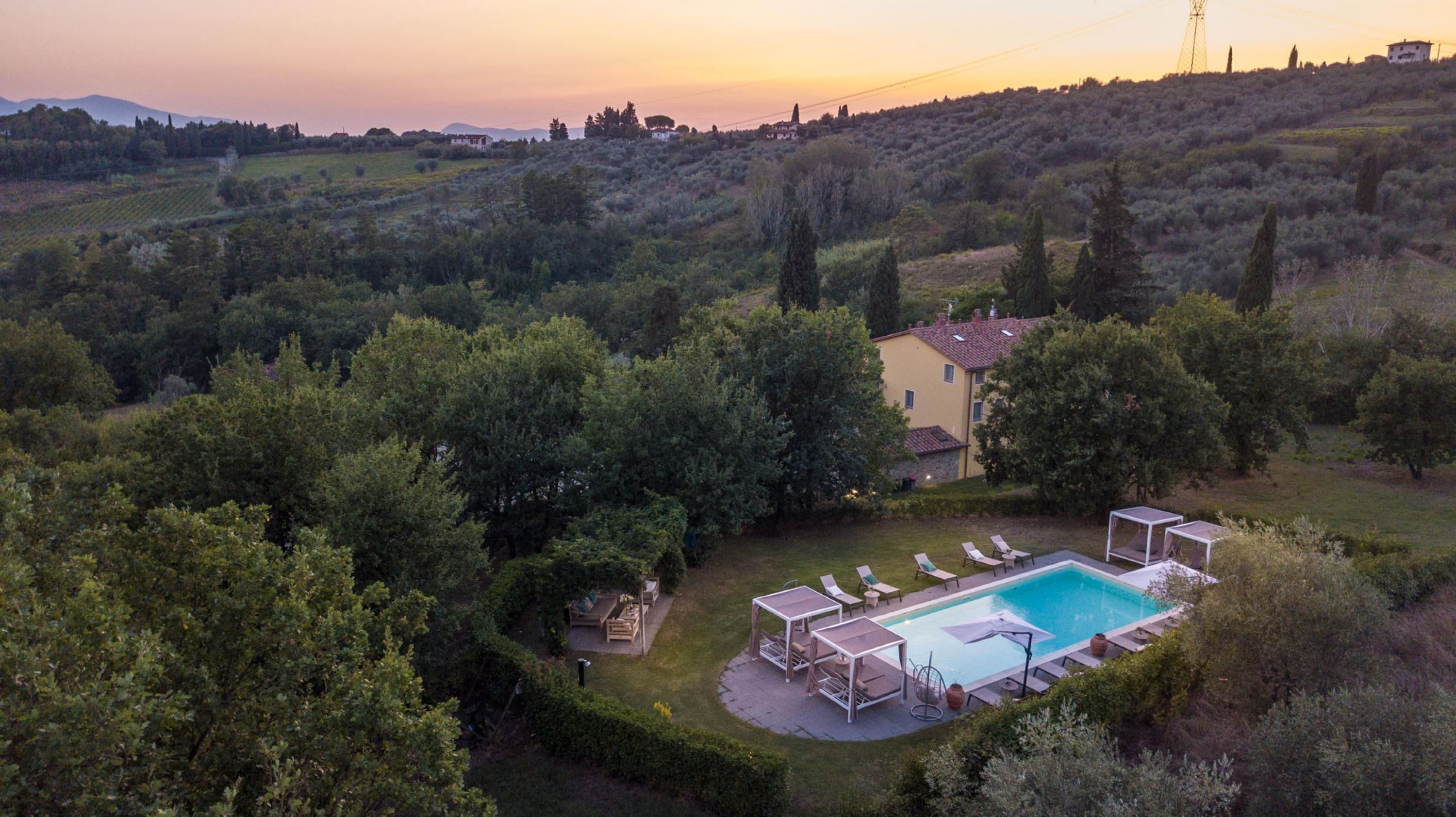 A villa with a swimming pool surrounded by lush greenery and hills in the background.
