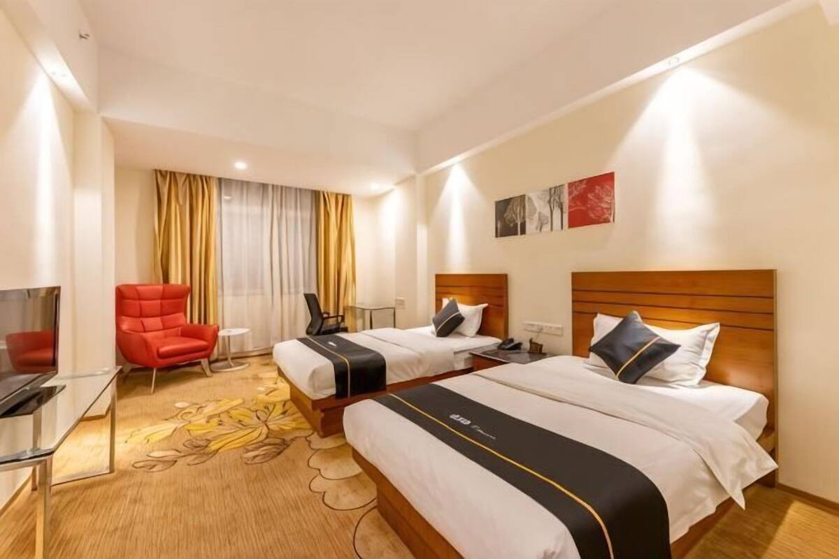 A hotel room with two beds, a TV, a red chair, and a window with curtains.