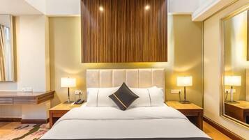 A hotel room with a large bed, bedside tables with lamps, a wooden ceiling panel, and a large mirror on the wall.