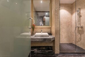 Une salle de bain moderne avec une douche à parois de verre, un lavabo surmonté d’un plan de travail en marbre et un grand miroir.