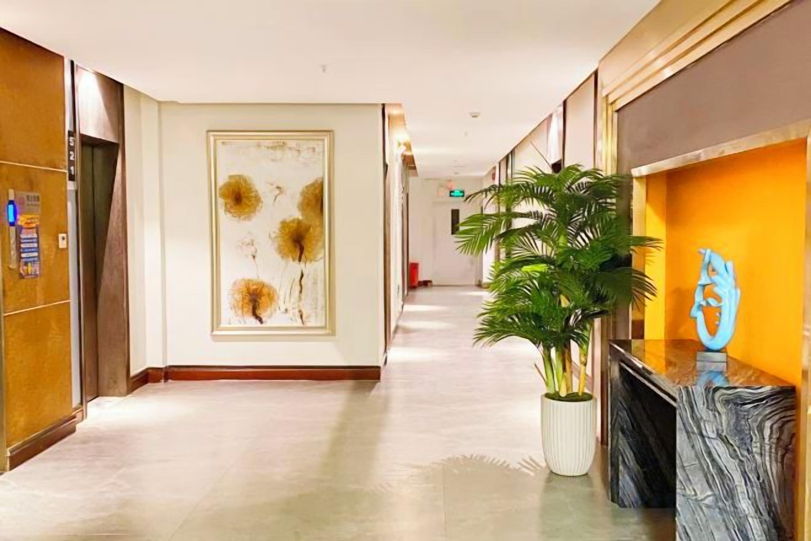 Un couloir d’hôtel avec un comptoir d’accueil, une plante en pot et une œuvre d’art accrochée au mur.