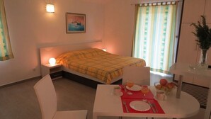 A hotel room with a bed, bedside table with a lamp, a dining table set for breakfast, and a window with curtains. - Studio apartment in Orebić with Seaview, Balcony, Air condition, WIFI (4202-1) (Orebic)