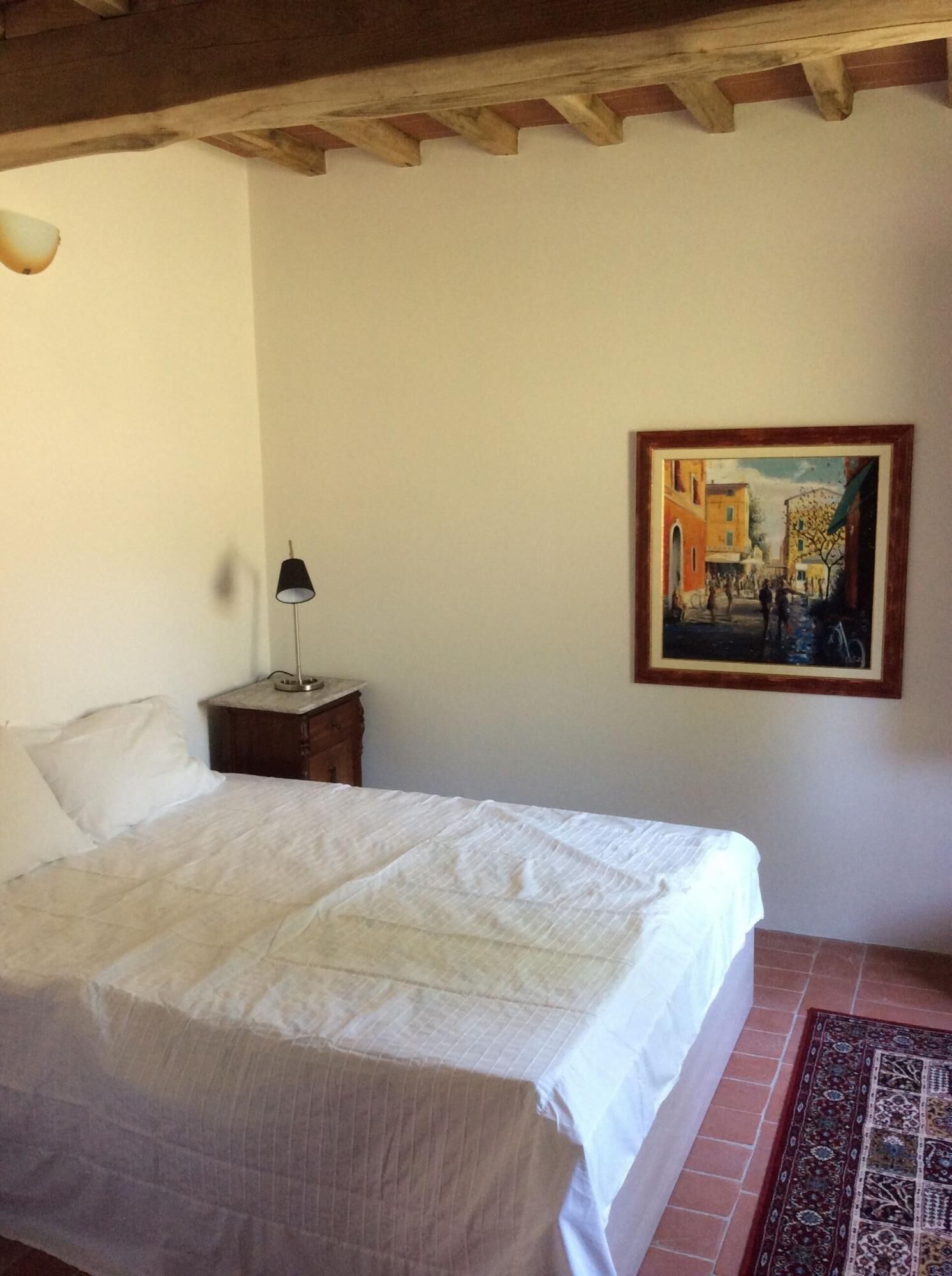 A bedroom with a bed, a nightstand, a lamp, and a painting on the wall.