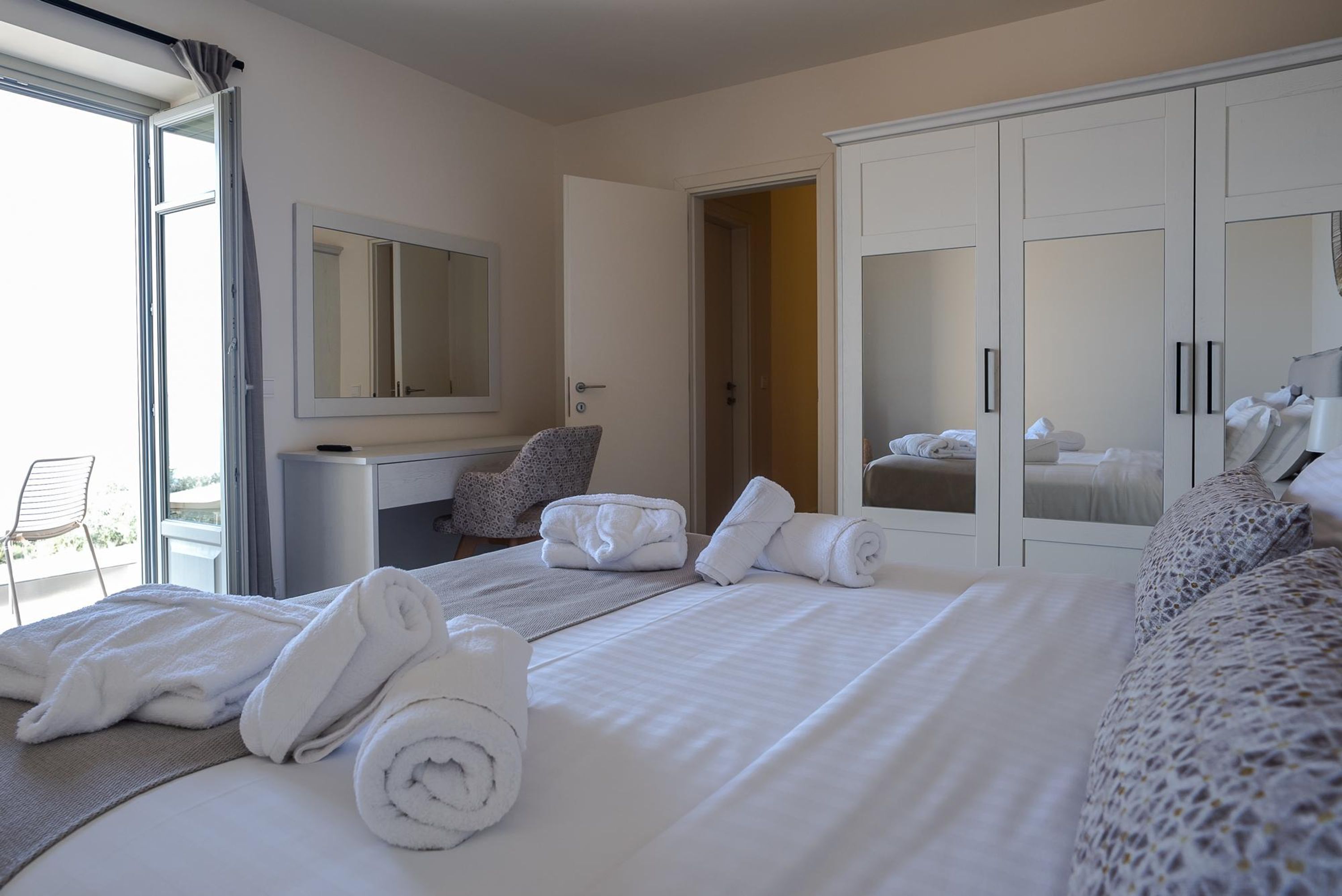 A hotel room with a large bed, a desk, a chair, and a wardrobe.