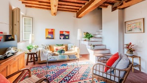 A cozy living room with a sofa, coffee table, and a patterned rug. There is a staircase with a railing and a plant on a side table. - Casa Noscali at Borghetto Farmhouse (Capannori)