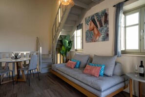 A modern living room with a sofa, dining table, chairs, a staircase, and a large window. - Villa Stoupa Exclusivity (West Mani)