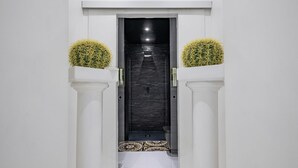 A modern hallway with a dark wall, white columns, and a patterned floor leading to a door.