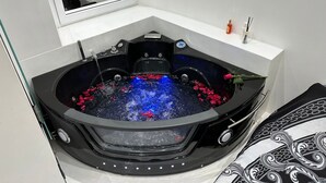 A corner bathroom with a black jacuzzi tub, a white bathtub, and a mirror above the tub.