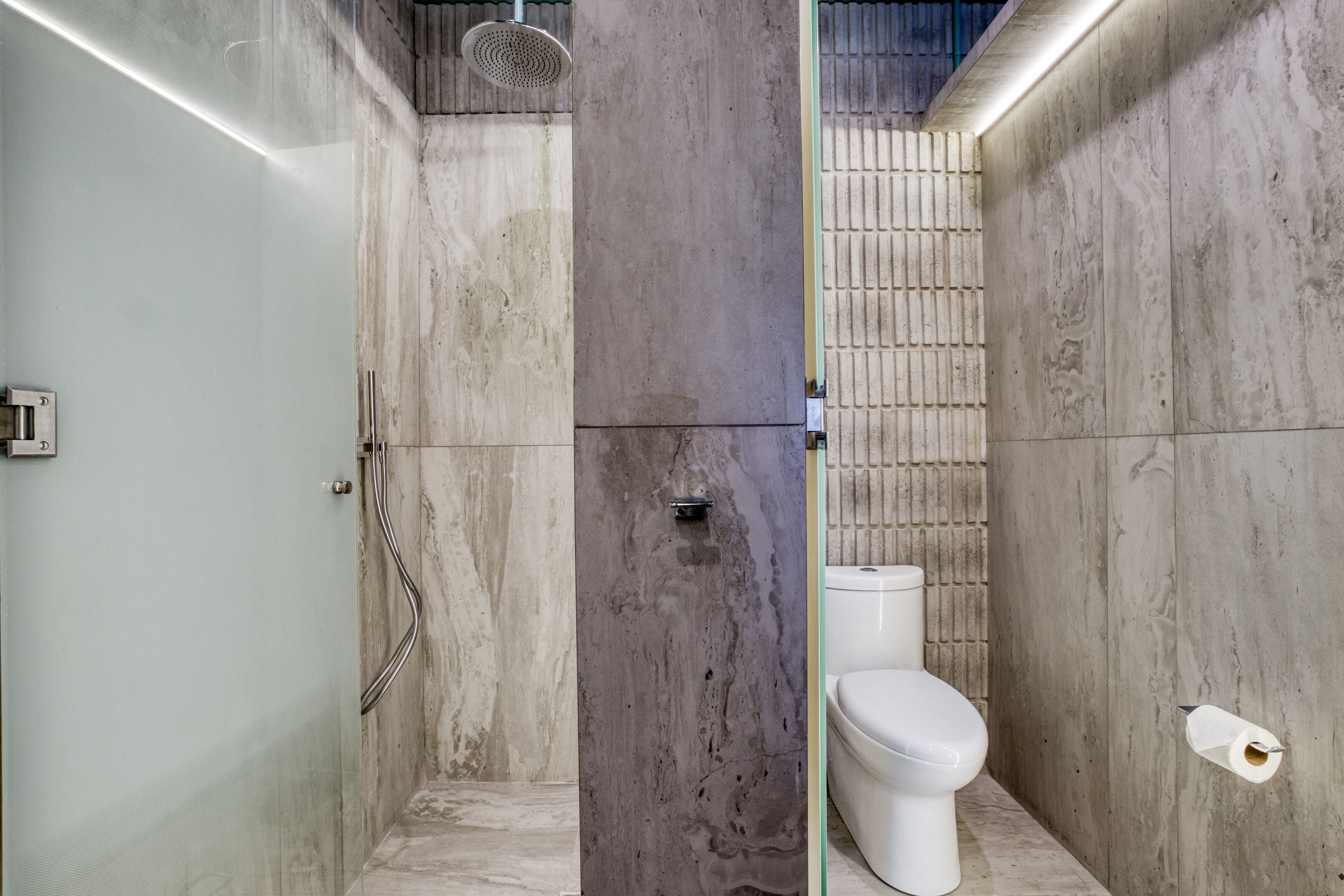 A bathroom with a shower, toilet, and marble walls.