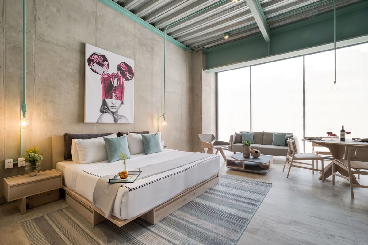 A modern bedroom with a large bed, a dining area, and a view of the sky.