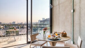 Un balcón con una mesa redonda dispuesta para el desayuno, un florero con flores y vistas a la ciudad.
